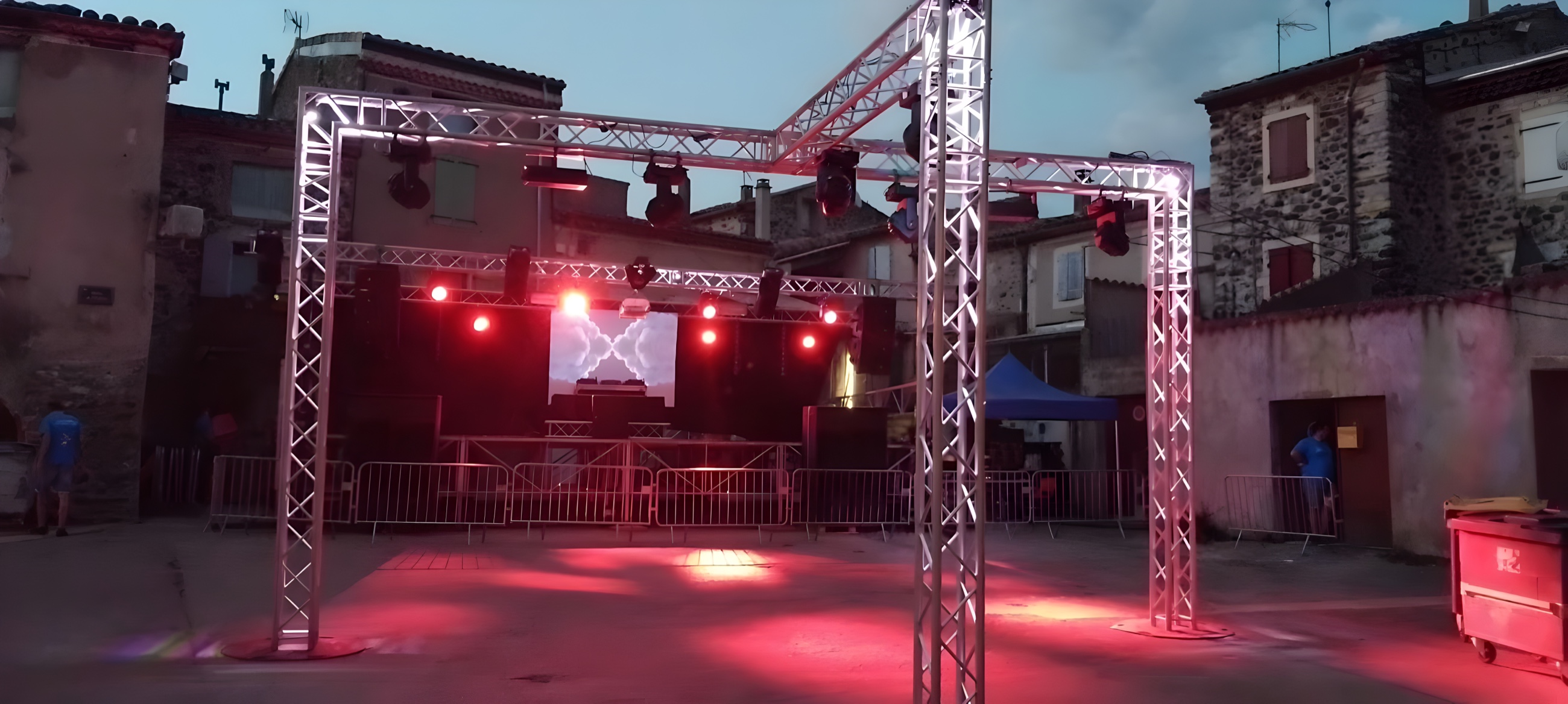 Portique de structures et scène éclairés en rose sur la place d'un village au crépuscule